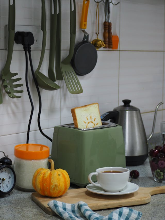 A slice of toast with a sun design popping out of a green toaster in a kitchen setting.