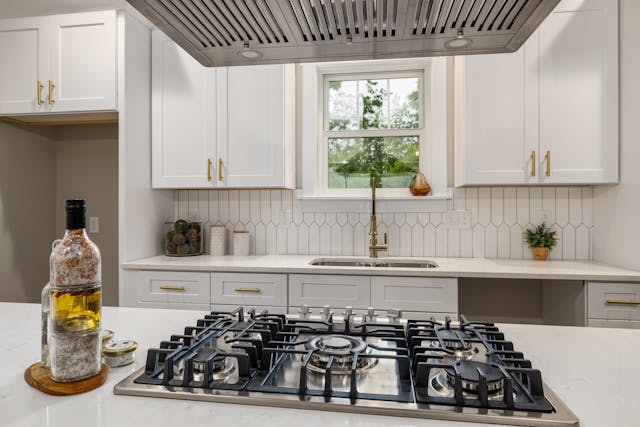 Modern white kitchen with a built-in stainless steel gas stove hob beneath a ceiling-mounted range hood.