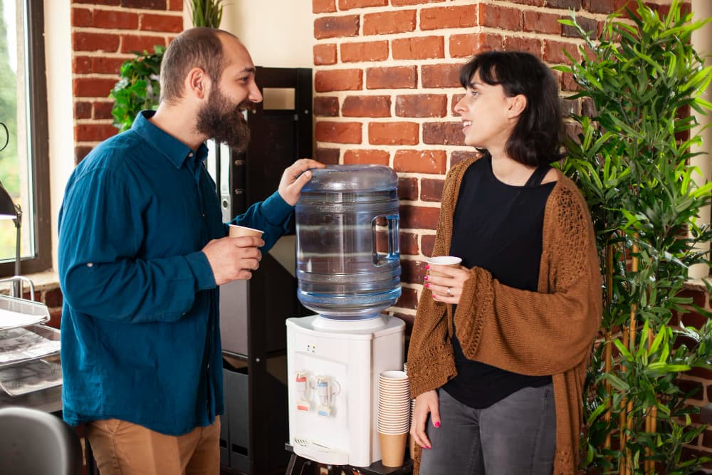 Two people enjoying safe drinking water from a modern water dispenser in an office space