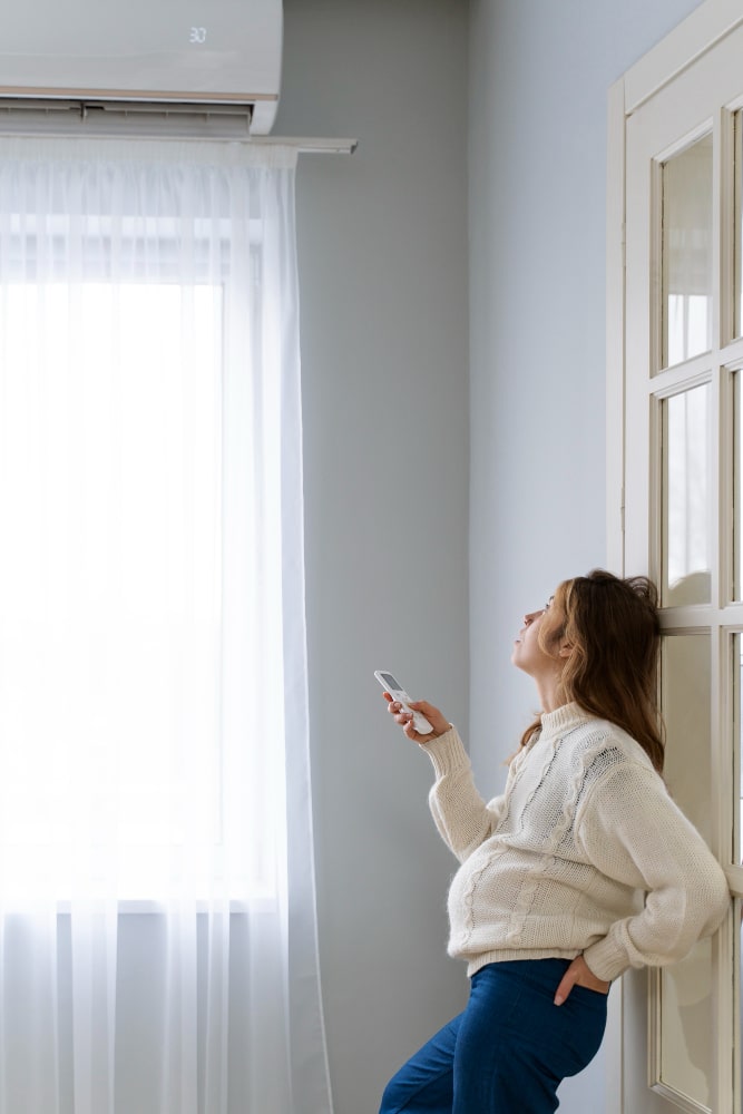 Woman using wall-mounted air conditioner in bright modern living room